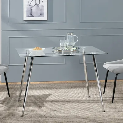 A glass-top dining table with chrome legs, set in a room with grey walls and a rug.