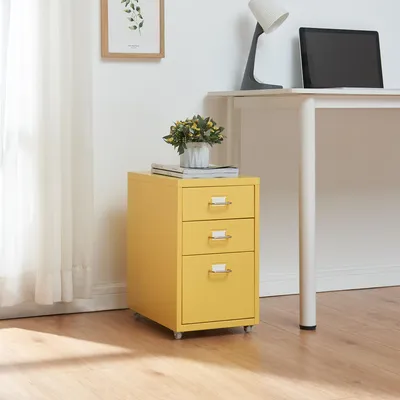 A yellow metal filing cabinet with three drawers is placed next to a white desk. A plant in a pot sits on top of the cabinet.