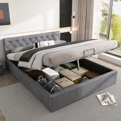 A grey upholstered bed with its storage compartment open, revealing stored items, in a well-lit bedroom with a large window.