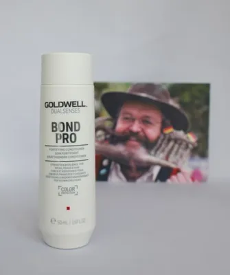 A bottle of Goldwell Dualsenses Bond Pro Conditioner is placed in front of a framed photograph of a man.