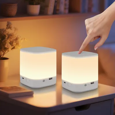 A hand is shown touching a bedside lamp on a nightstand, with another lamp in the background.