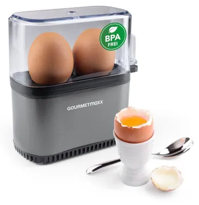 A GOURMETmaxx egg cooker with two eggs inside, and a cooked egg in an egg cup next to it.