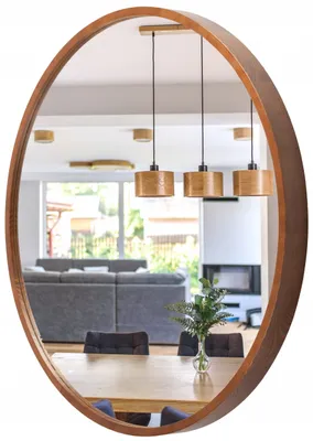 A round mirror with a wooden frame reflects a dining area and living room with furniture and pendant lights.