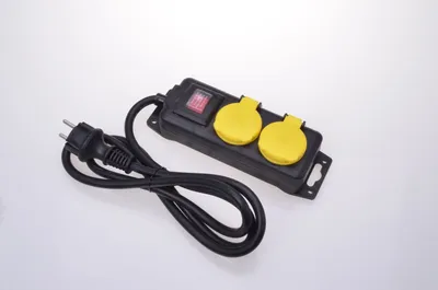 A black power strip with two yellow outlets and a red switch, lying on a white background.