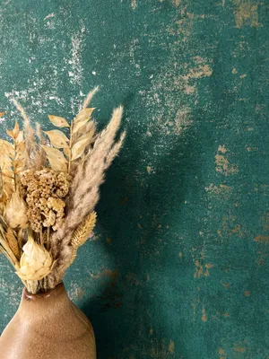 A bouquet of dried flowers in a vase against a textured green and gold background.