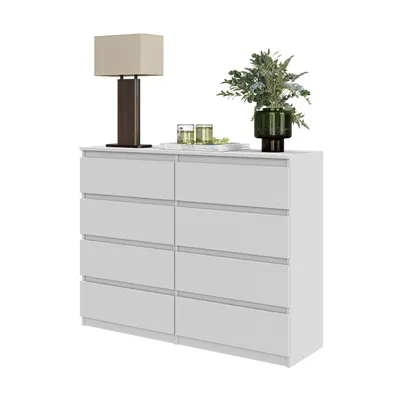 A white dresser with eight drawers, a lamp, and a vase with greenery on top, isolated on a white background.