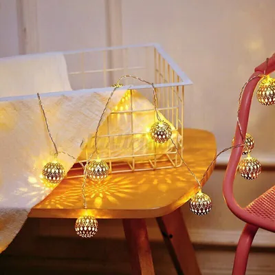 A string of decorative lights with spherical, filigree shades is draped over a table and a pink chair.
