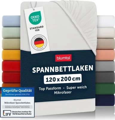 A stack of folded fitted sheets in various colors, with a white fitted sheet prominently displayed in the foreground with product information tags.