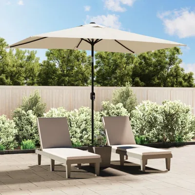 Two lounge chairs and a patio umbrella are set up on a paved patio area, surrounded by lush green bushes and a wooden fence.