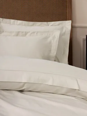 A close-up view of white bedding, including pillows and a duvet, on a bed with a woven headboard.