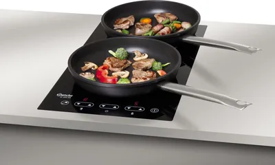 Two frying pans with food cooking on an induction cooktop.