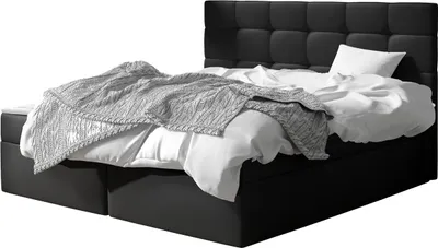 A black upholstered boxspring bed with a white mattress and a gray knitted throw blanket.
