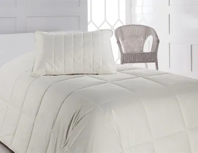 A bed with a pillow and a comforter, with a wicker chair in the background.