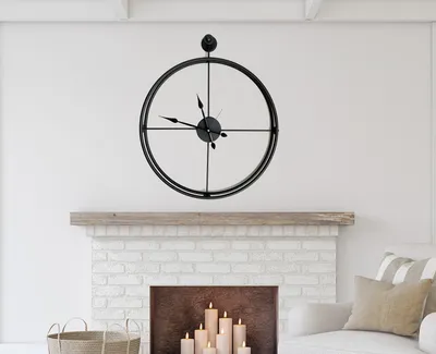A black metal wall clock is mounted on a white wall above a fireplace.