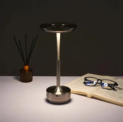 A modern LED desk lamp is shown on a white surface next to an open book and a diffuser.