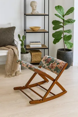 A living room scene with a rocking footrest in the foreground and shelves with decor and plants in the background.