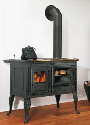 A black cast iron wood-burning stove with a chimney pipe, a kettle on top, and bread in the oven.