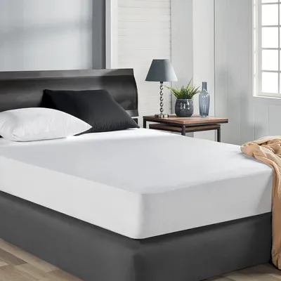A bed with white sheets, a black pillow, and a white pillow, with a bedside table and lamp.