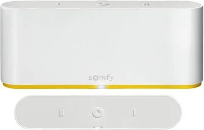A white Somfy Tahoma Switch smart home hub and its remote control are shown against a white background.