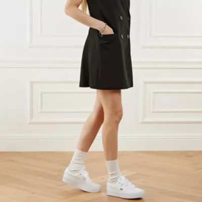 A person wearing a black dress and white sneakers with white socks.