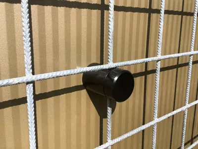 A close-up shot of a black plastic spacer attached to a white wire fence.