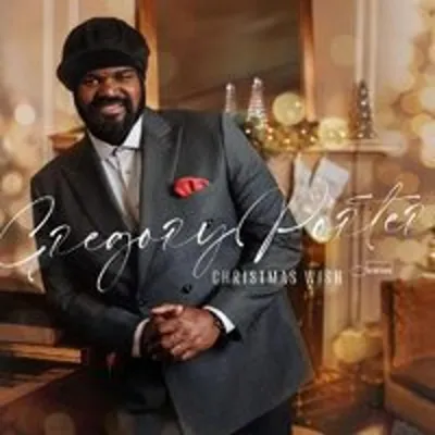 A man in a suit is posing in front of a fireplace decorated for Christmas.