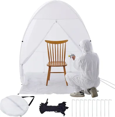 A person in a protective suit is spraying a chair inside a white pop-up spray booth.