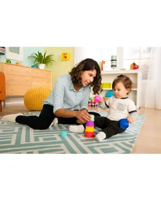 A woman and a baby are playing with stacking cups on a rug.