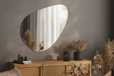 A decorative mirror is displayed on a wall above a wooden cabinet, adorned with dried flowers and decorative items.