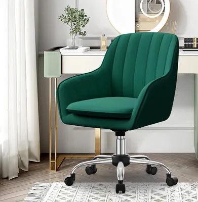 A green velvet office chair is shown in a well-lit room, possibly a home office or dressing area, with a vanity table and curtains in the background.