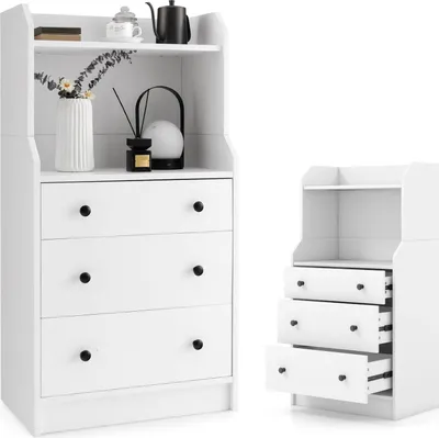 A white wooden dresser with three drawers and an open shelf above, shown next to a smaller, identical dresser unit. The larger dresser has decorative items on the top shelf and in the open compartment.