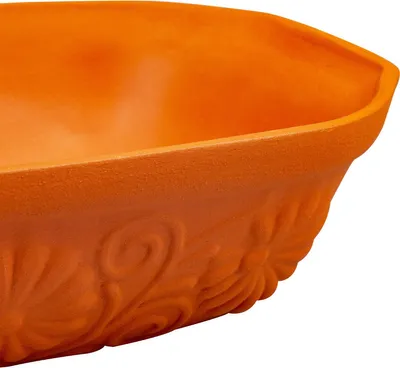 A close-up view of the side of an orange ceramic pot with embossed floral patterns.