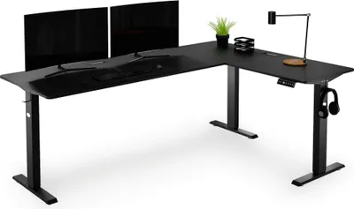 A black L-shaped standing desk with two monitors, a lamp, and headphones.