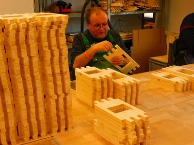 A man is assembling wooden components of what appears to be a birdhouse kit in a workshop setting.