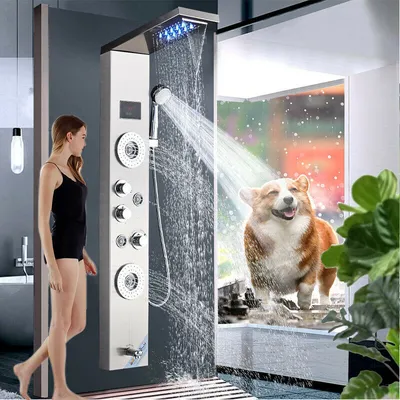 A woman stands next to a modern shower panel while a happy corgi dog stands in a shower with water falling.