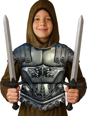 Ein lächelndes Kind in einem goldbraunen Kettenhemd trägt eine silberne Gladiator-Rüstung und hält zwei Spielzeug-Schwerter in den Händen, jeweils eines links und rechts.