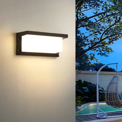 An outdoor wall light illuminates a textured wall next to a patio with a hanging chair and a pool.