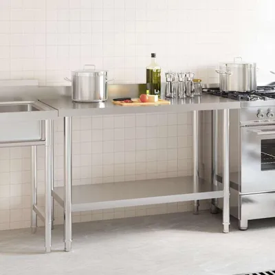 A stainless steel kitchen work table with a sink and a stove in the background.