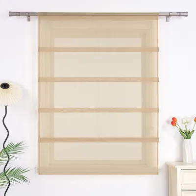 A beige sheer Roman blind with horizontal bands hangs in front of a window. A lamp and plants are visible to the left, and a vase of tulips sits on a cabinet to the right.