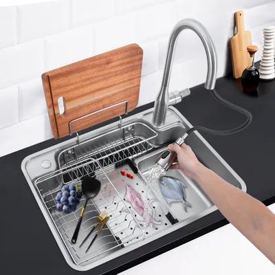 A person is using a pull-out faucet to rinse food in a kitchen sink.