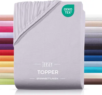 A stack of folded jersey topper bed sheets in various colors, with a light gray sheet prominently displayed in the foreground.
