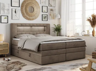 A bedroom scene with a large boxspring bed as the focal point, decorated with artwork and plants.