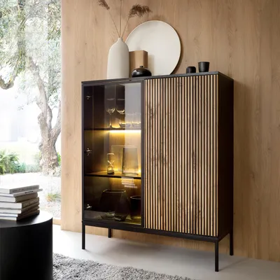 A modern vitrine with glass doors and wooden slatted doors, displaying decorative items, in a room with wooden walls and a rug.