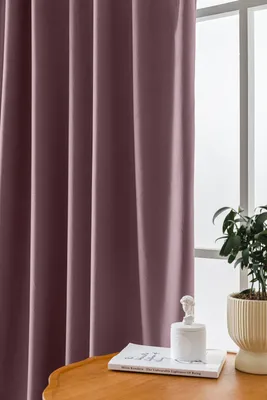 A close-up view of a pink velvet curtain hanging next to a window. A small white statue and a potted plant are visible on a wooden table in the foreground.