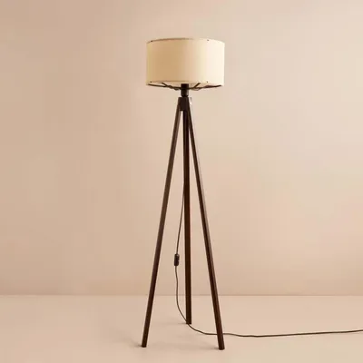 A floor lamp with a tripod base and a fabric shade against a plain background.