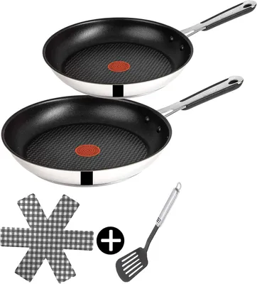 Two frying pans are stacked on top of each other, with a pan protector and a spatula below.