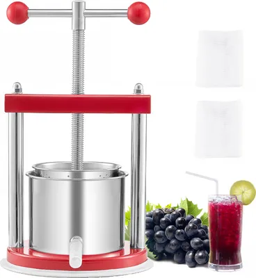 A red and silver fruit press with grapes and a glass of juice next to it.