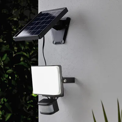 A solar-powered outdoor light with a motion sensor is mounted on a wall.