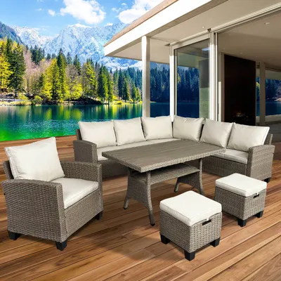 A polyrattan corner seating group with a table and ottomans on a wooden deck, with a scenic lake and mountain backdrop.