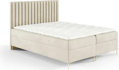 A beige upholstered boxspring bed with a white mattress topper and gold legs, shown against a white background.